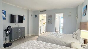 Ein Schlafzimmer mit zwei Betten, einem Fernseher, einer Kommode und einer Tür zu einem Badezimmer.