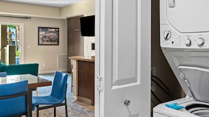 Een wasruimte met een voorlader wasmachine en droger, een eethoek met stoelen en uitzicht buiten via een deur.