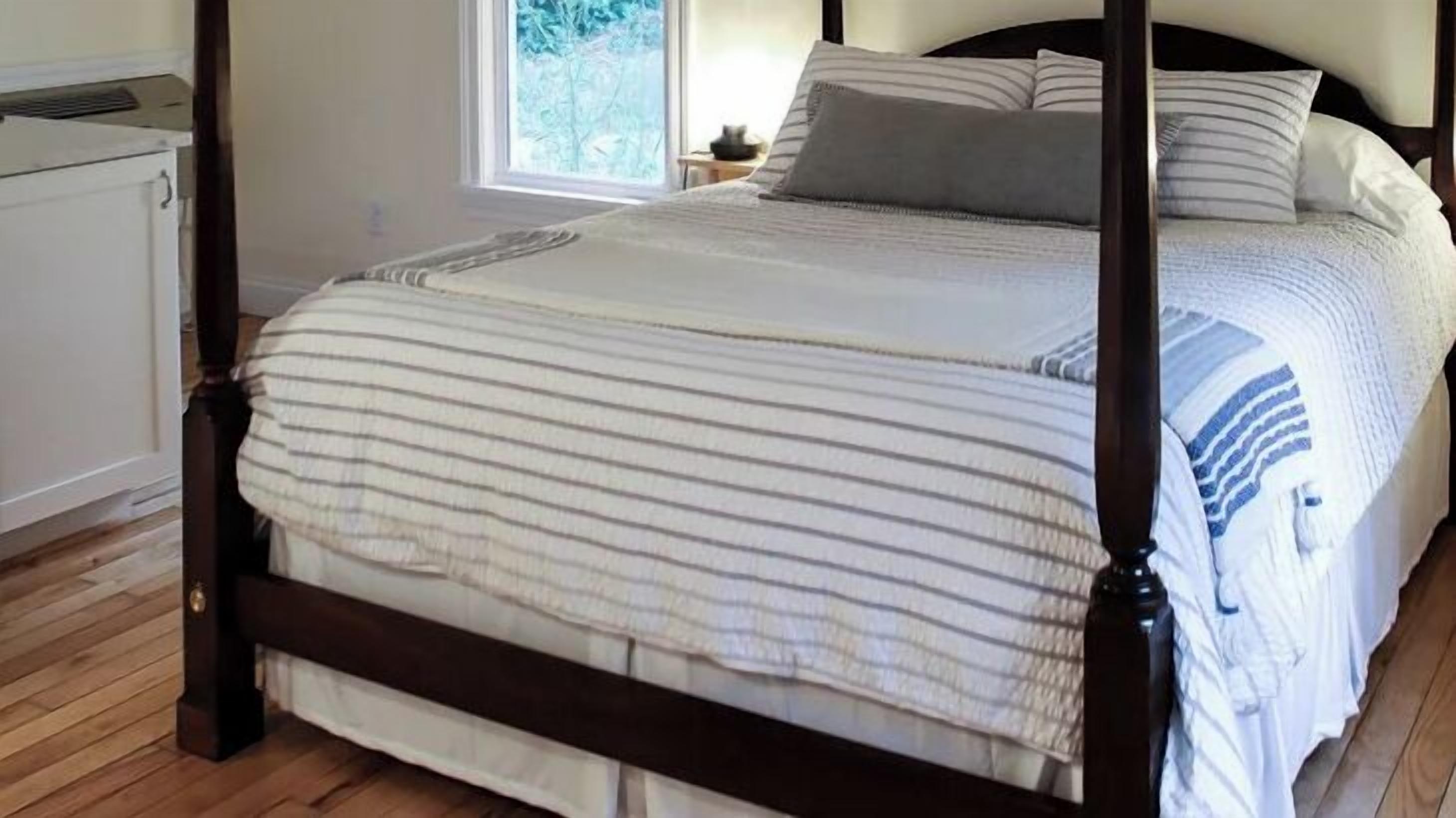 Un lit à baldaquin avec une couvre-lit à rayures, un plancher en bois et une fenêtre donnant sur les arbres.