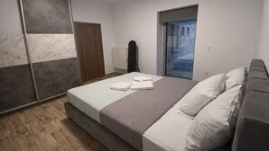 A bedroom with a bed, a wardrobe, a radiator, and a view of a blue sky and a building. - AG Stone Home - Idyllic Beachside Villa in Isthmia (Loutraki-Agioi Theodoroi)