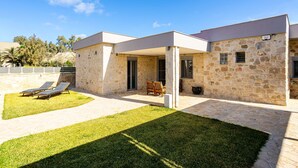 A modern house with a stone facade, a covered patio, and a lawn with sun loungers. - AG Stone Home - Idyllic Beachside Villa in Isthmia (Loutraki-Agioi Theodoroi)