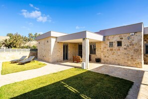 A modern house with a stone facade, a covered patio, and a lawn with sun loungers. - AG Stone Home - Idyllic Beachside Villa in Isthmia (Loutraki-Agioi Theodoroi)