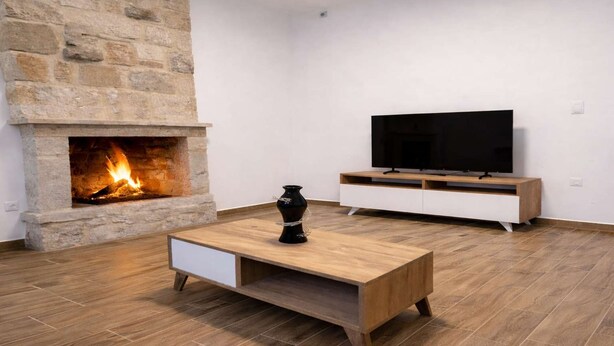A modern living room with a stone fireplace, a wooden coffee table, a white TV stand, and a flat-screen TV. - AG Stone Home - Idyllic Beachside Villa in Isthmia (Loutraki-Agioi Theodoroi)