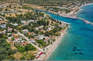 An aerial view of a coastal town with residential buildings, a beach, and a marina. - AG Stone Home - Idyllic Beachside Villa in Isthmia (Loutraki-Agioi Theodoroi)