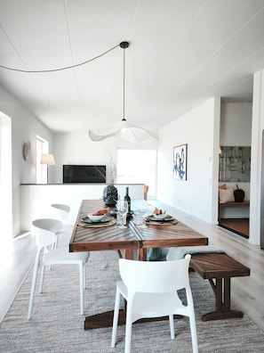A modern dining area with a wooden table, white chairs, and a unique ceiling light fixture.