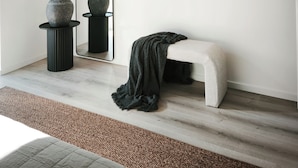 Une pièce au décor minimaliste, avec un grand miroir, un banc et deux vases posés sur un piédestal.