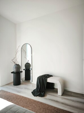 Une pièce au décor minimaliste, avec un grand miroir, un banc et deux vases posés sur des piédestaux.