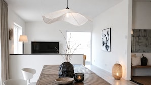 Un espace de repas moderne avec une table en bois, des chaises blanches, un vase avec des branches, une bougie et un luminaire suspendu.