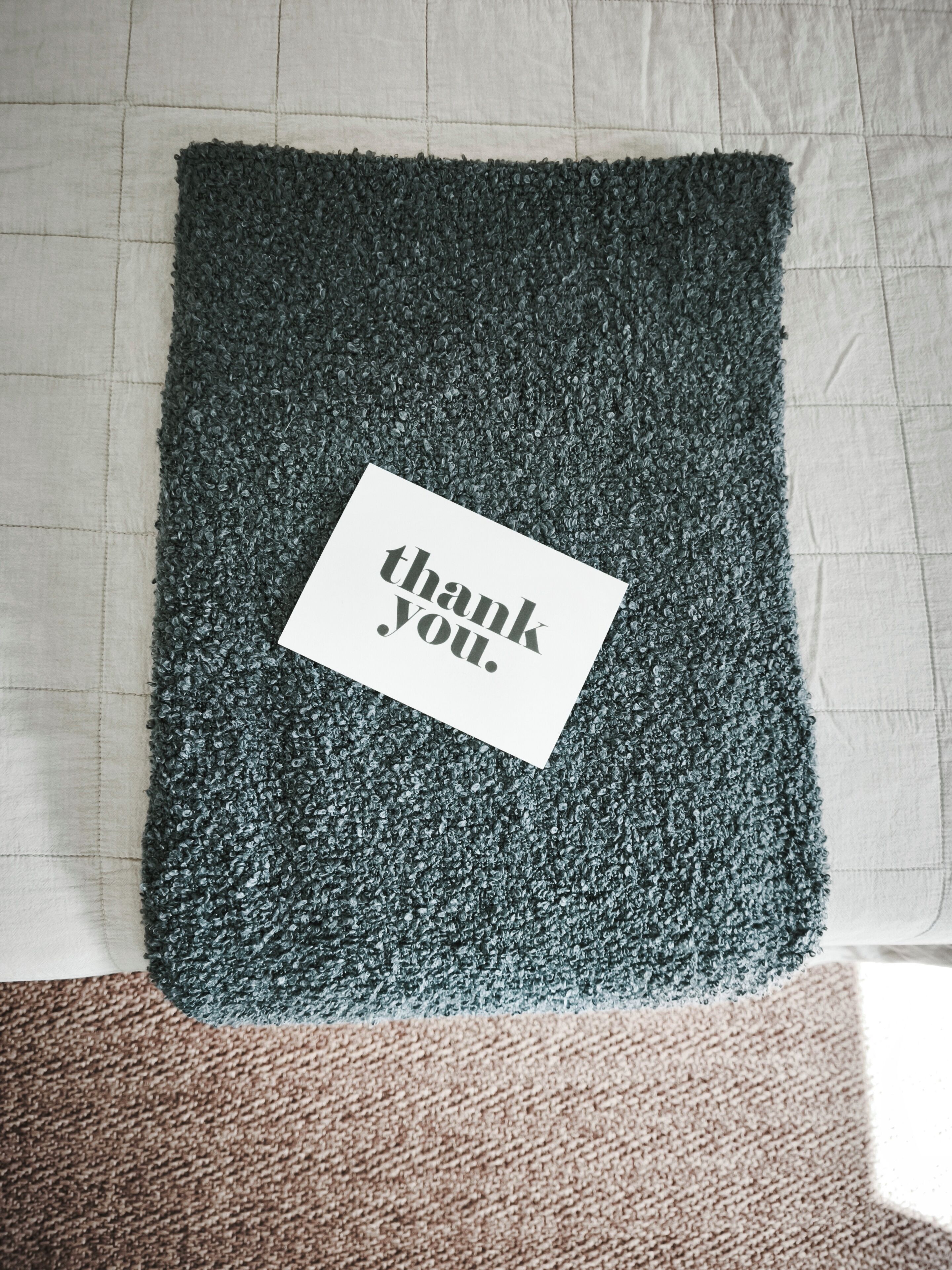 Un tapis vert foncé à texture marquée, sur lequel est posée une carte de remerciement.