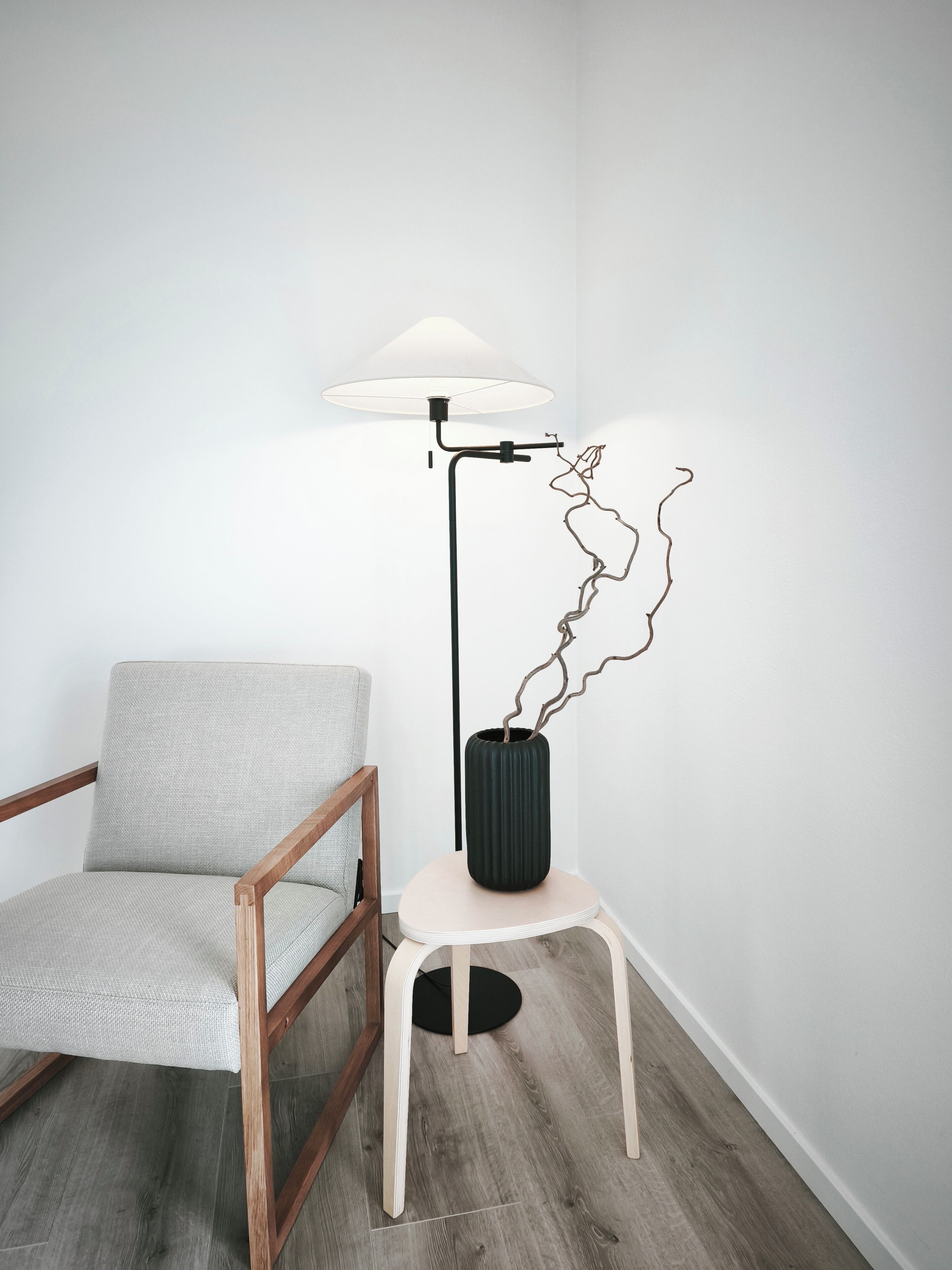 A modern chair, a floor lamp, and a vase with a branch.