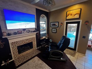Ein Wohnzimmer mit Kamin, Fernseher, Liegesessel und Blick auf einen Swimmingpool.