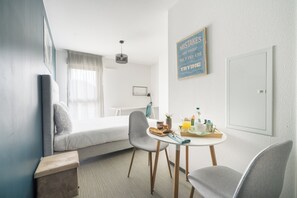 Ein modernes Hotelzimmer mit Bett, Esstisch mit Frühstücksangebot, Stuhl und einem an der Wand befestigten Schild.