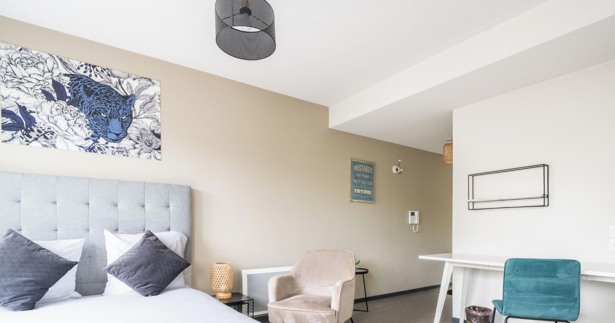 A hotel room with a bed, a chair, a desk, and a wall with a poster.