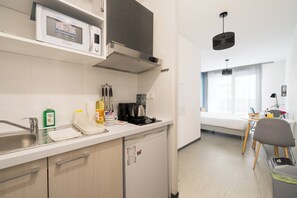 Une cuisine compacte équipée d’un four à micro-ondes, d’un grille-pain et d’une machine à café. Elle comprend un coin repas avec une table et des chaises, ainsi qu’une fenêtre avec des rideaux.