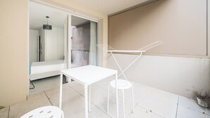 Ein kleiner Balkon mit weißem Tisch und Stuhl, einer hängenden Lampe und einem Blumentopf.