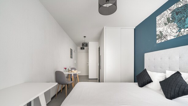 Ein modernes Hotelzimmer mit Bett, Schreibtisch, Sessel und kleinem Tisch.