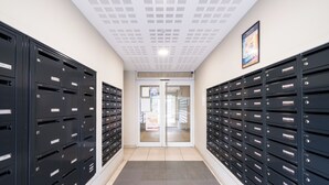 Ein Korridor mit Reihen schwarzer Briefkästen, einem Kachelboden und einer Doppeltür am Ende.
