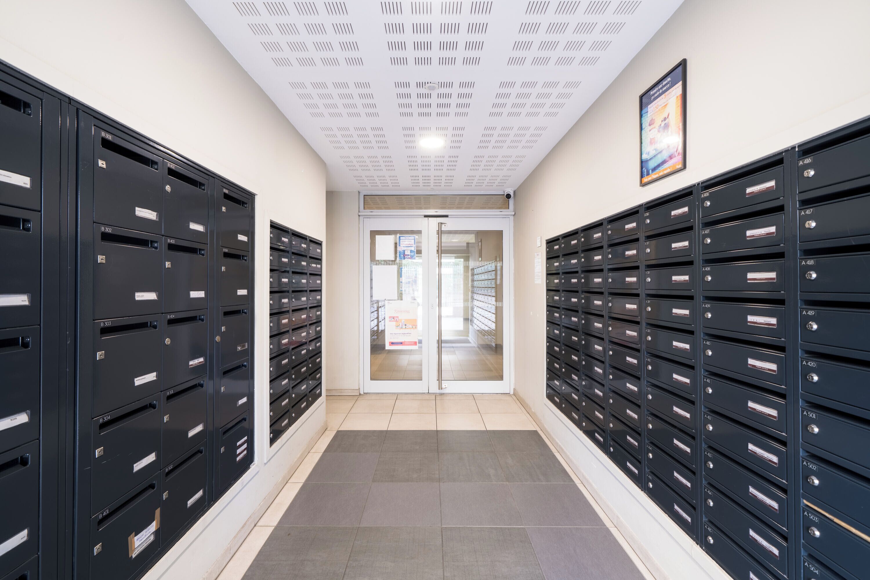 A hallway with rows of black mailboxes, a tiled floor, and a double door at the end.