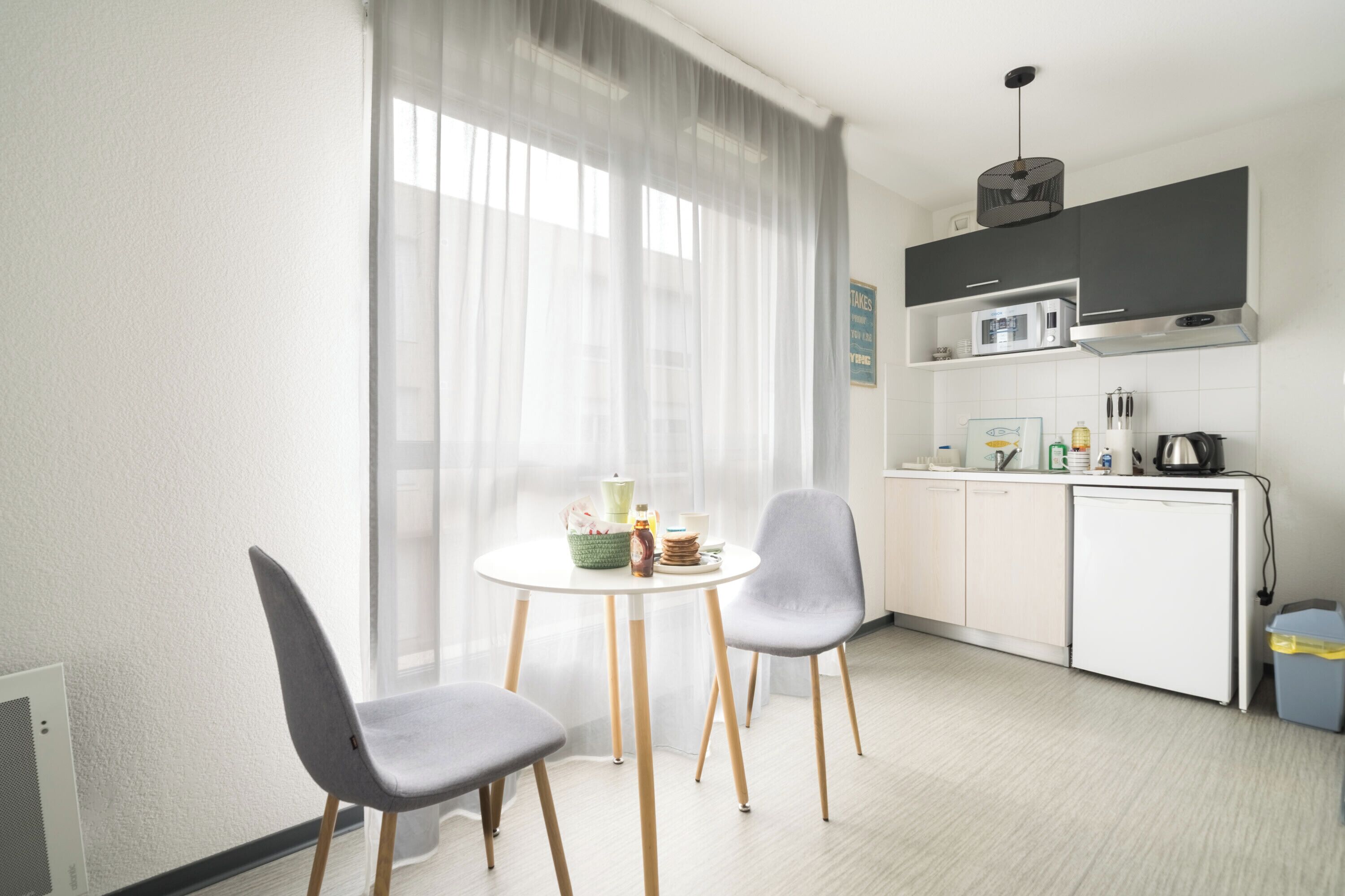Une cuisine moderne avec un coin repas, comprenant une table blanche avec des chaises, un four à micro-ondes et un évier.