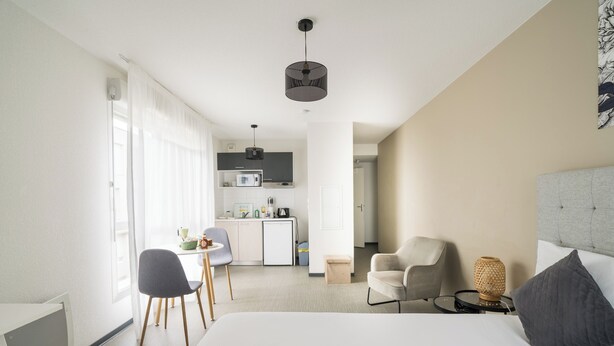 A modern hotel room with a bed, a desk, a chair, a small kitchen area, and a dining table. - A308 - Le Soléa - Wifi - Proche tram (Montpellier)