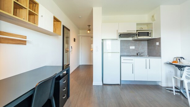 A modern kitchen with white cabinets, a microwave, and a refrigerator. There is a dining area with a table and chairs. - 402 - L'Herblinois - Wifi - Proche tram (Saint-Herblain)