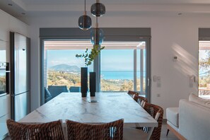 Ein moderner Essbereich mit einem Marmortisch, Korbstühlen und Meerblick.