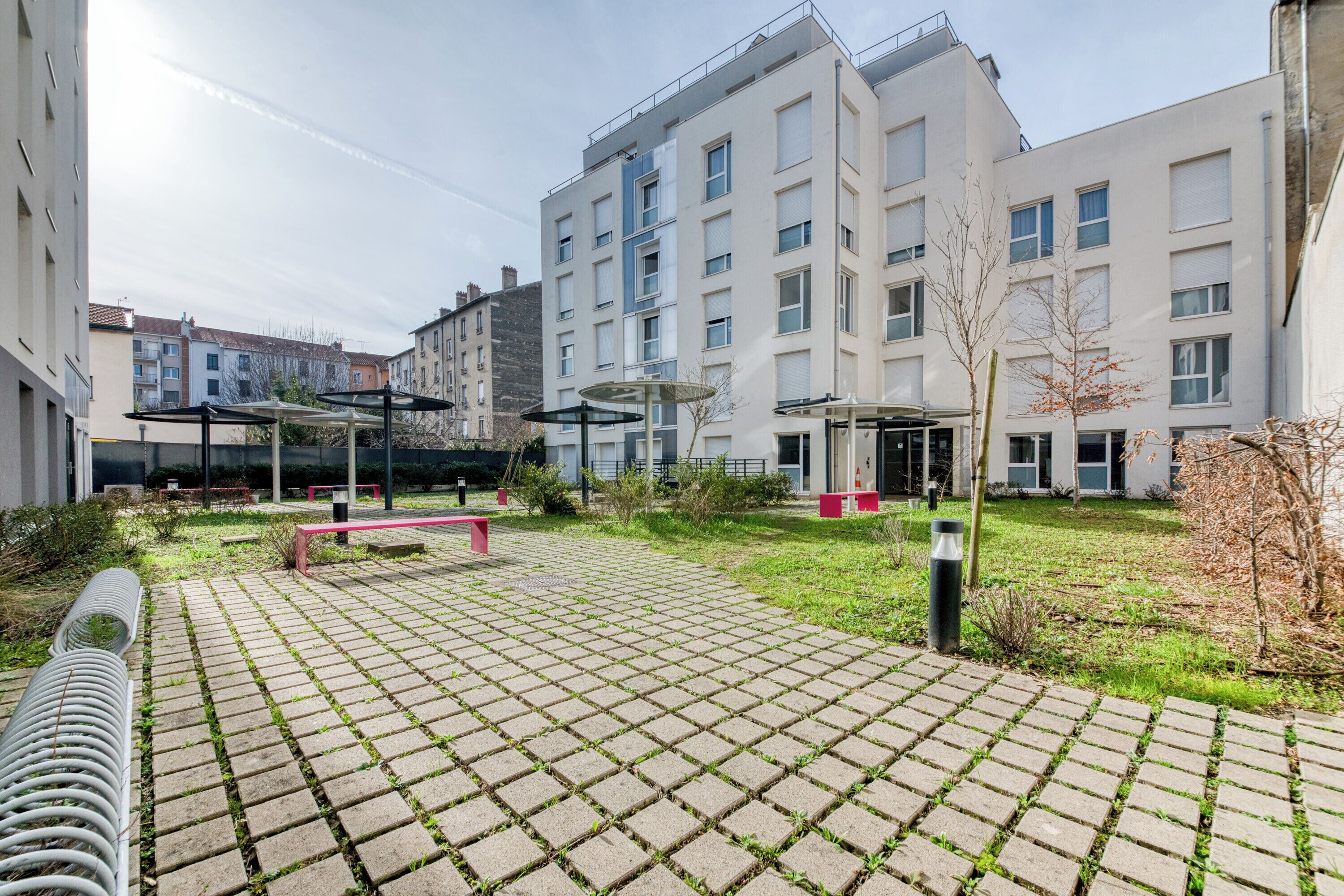 Un patio con sendero empedrado, mobiliario exterior y edificios modernos al fondo.