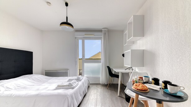 Une chambre d’hôtel avec un lit, un bureau, une chaise, une table sur laquelle se trouve une pizza, une tasse et une tasse à café.