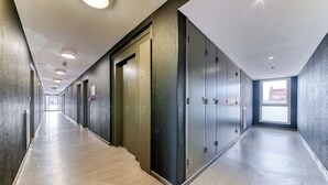 Un long couloir étroit doté d’un plancher en bois poli, de luminaires encastrés au plafond et d’une grande fenêtre au bout.