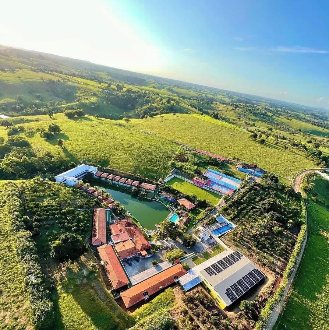 Vue aérienne d’une propriété dotée d’une piscine, de panneaux solaires et d’un grand bâtiment surmonté d’un toit rouge.
