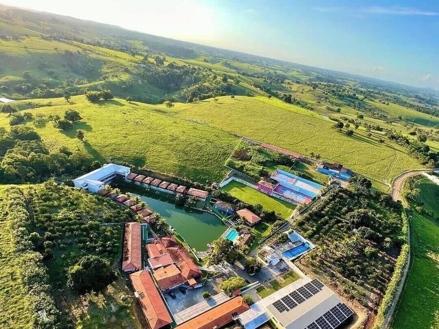 An aerial view of a property with a swimming pool, solar panels, and a large building with a red roof.