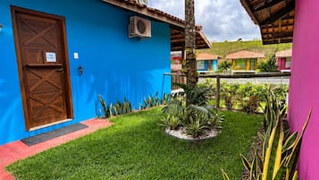 A blue building with a wooden door, a small garden with grass and plants, and a palm tree.