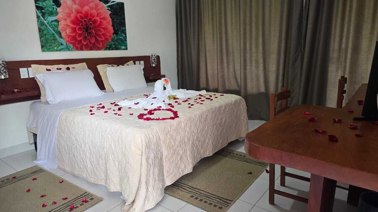 Ett hotellrum med en säng, en sänggavel i trä, ett matbord och en stor blomstermålning på väggen.