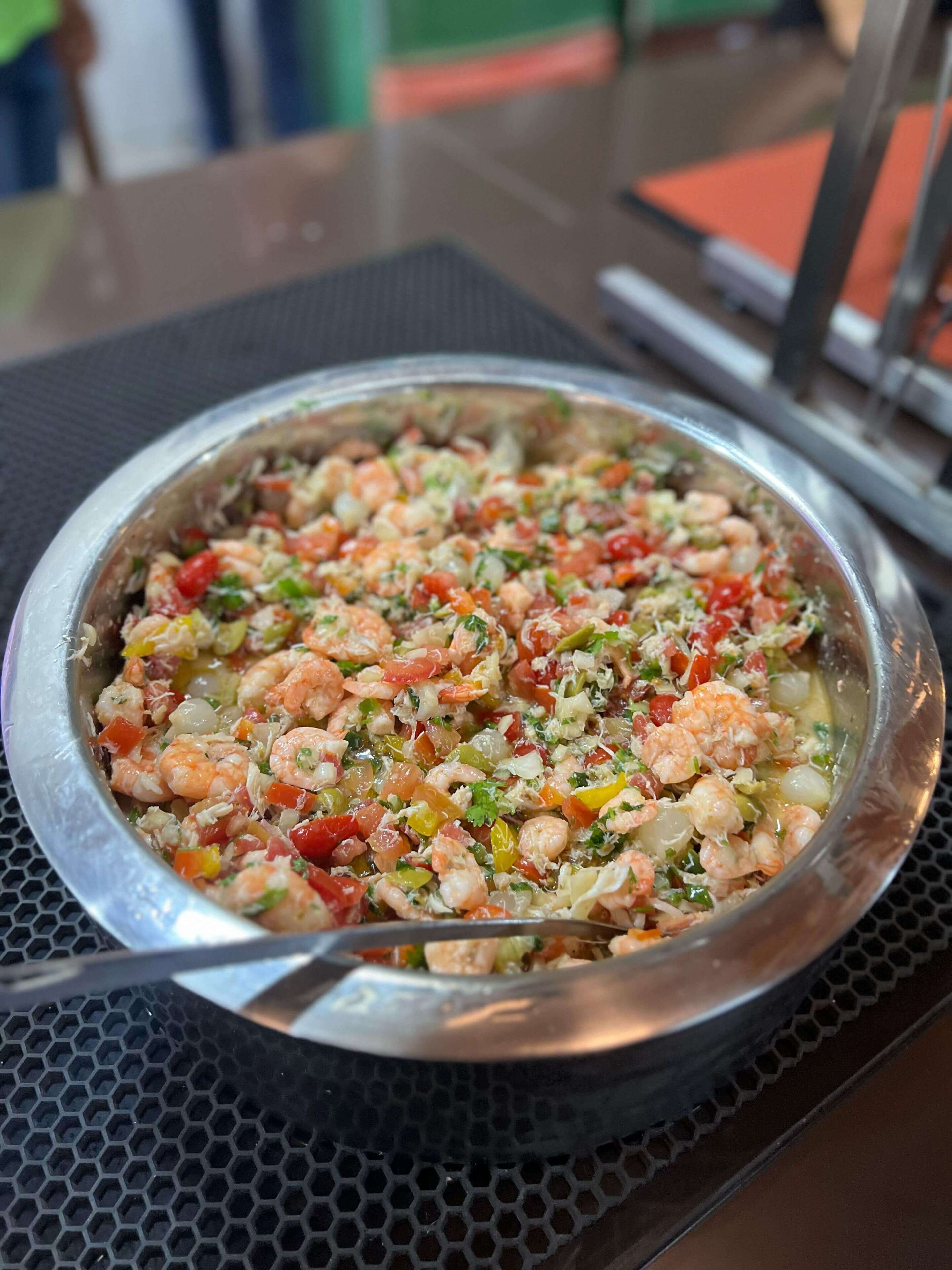 A seafood dish in a metal bowl on a table with a black mesh surface.