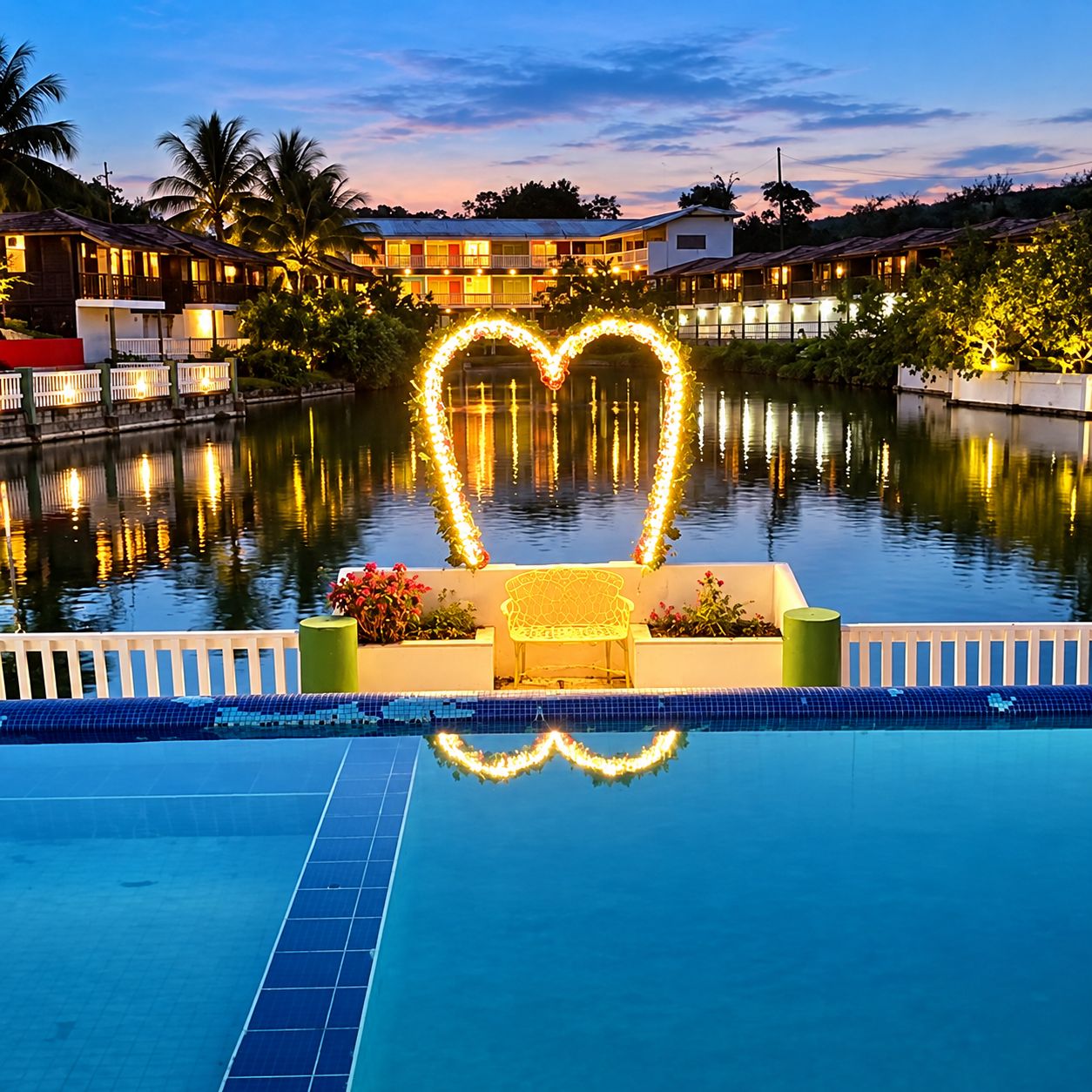 A swimming pool with a heart-shaped light decoration, surrounded by a white fence and a bench.