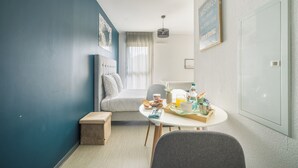 Een moderne hotelkamer met een bed, een eettafel met ontbijt, een klein krukje, een stoel en een groot raam.