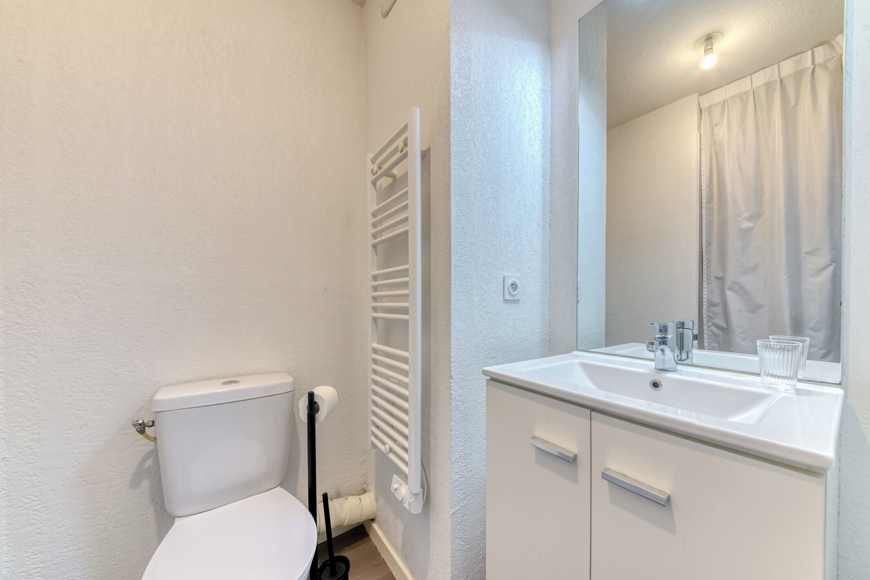 A bathroom with a toilet, a radiator, a sink with a mirror, and a glass.