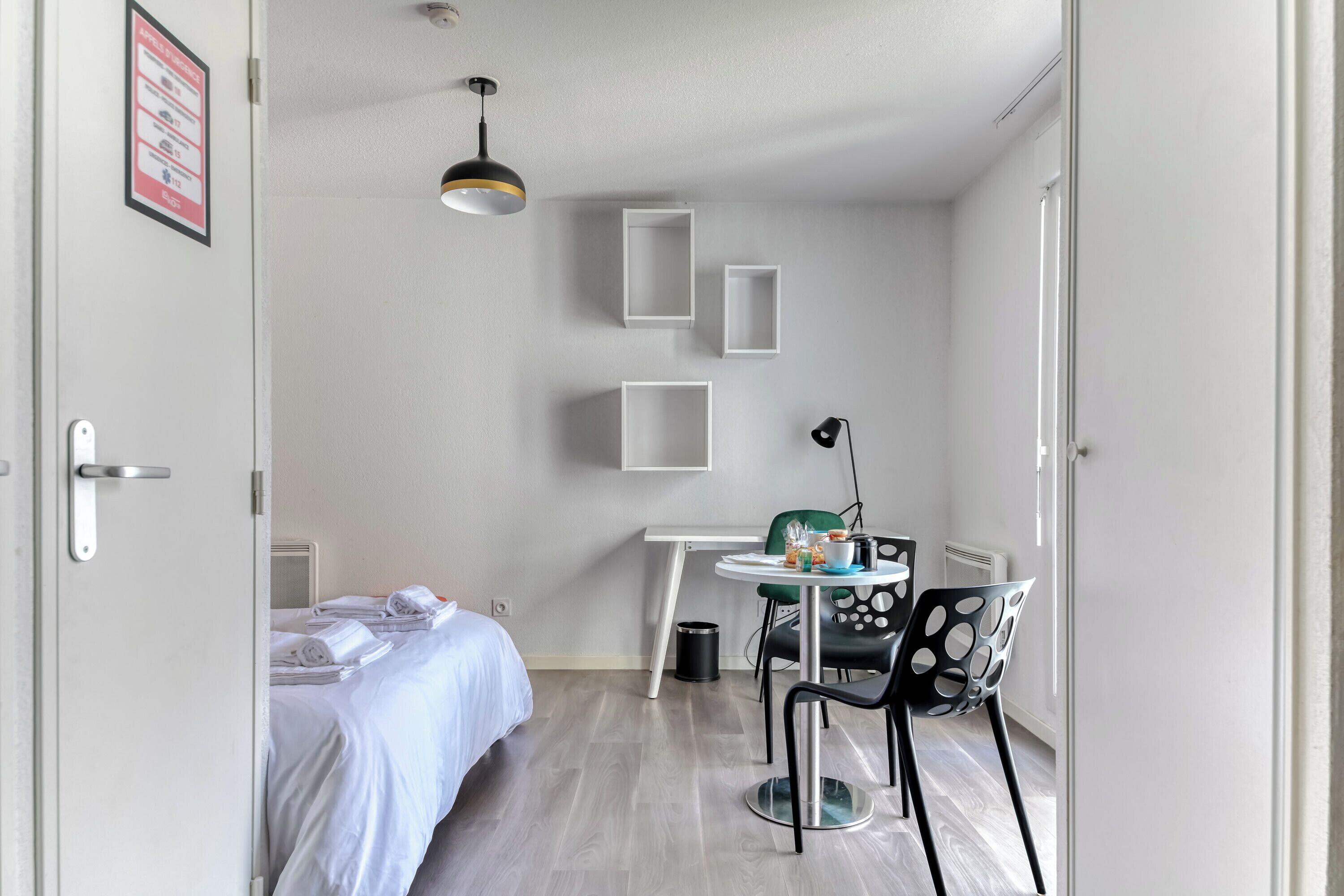 Een hotelkamer met een bed, een bureau, een stoel, een lamp en een wandplank.