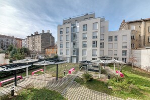 Un patio con asientos exteriores, un edificio con amplias ventanas y un camino pavimentado.