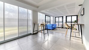 Ein geräumiges Zimmer mit großen Fenstern, einem blauen Sofa und einem kleinen Tisch mit Stühlen.