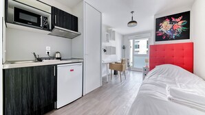 Eine moderne Küche mit Mikrowelle, Herd und Kühlschrank. Es gibt einen Essbereich mit Tisch und Stühlen. Im Vordergrund ist ein Bett mit rotem Kopfteil zu sehen.