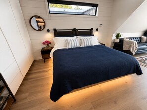 Ein Schlafzimmer mit Bett, Nachttisch, Spiegel und Fenster.