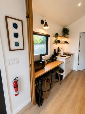 Een kleine keuken met een magnetron, koffiehoek en uitzicht op groen.