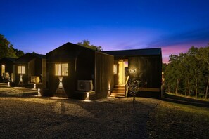 Een moderne, ruime houten hut met een grindpad, een kleine boom en een duidelijke trap naar de ingang.