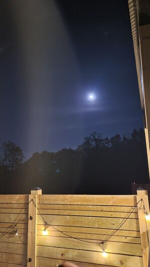 A wooden deck with string lights and a night sky with a visible moon. - Luna A-Frame | King Suite, Fire Pit & Hot Tub (Berkeley Springs)