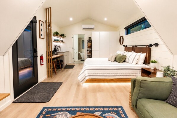 Un dormitorio con una cama, un escritorio, una silla, un sofá, una ventana y una puerta.