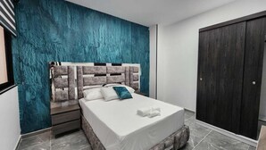 Un dormitorio moderno con una cama grande, un armario oscuro y una pared de acento color turquesa.
