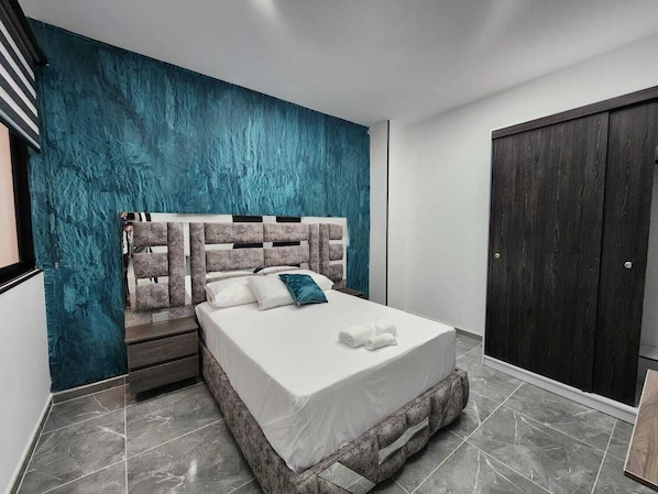 A modern bedroom with a large bed, a dark wardrobe, and a teal accent wall. - Hotel Boutique Batara (Filandia)