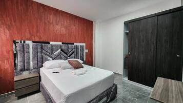 Une chambre à coucher moderne avec un lit, une tête de lit ornée d’un motif géométrique, une armoire et une petite table.