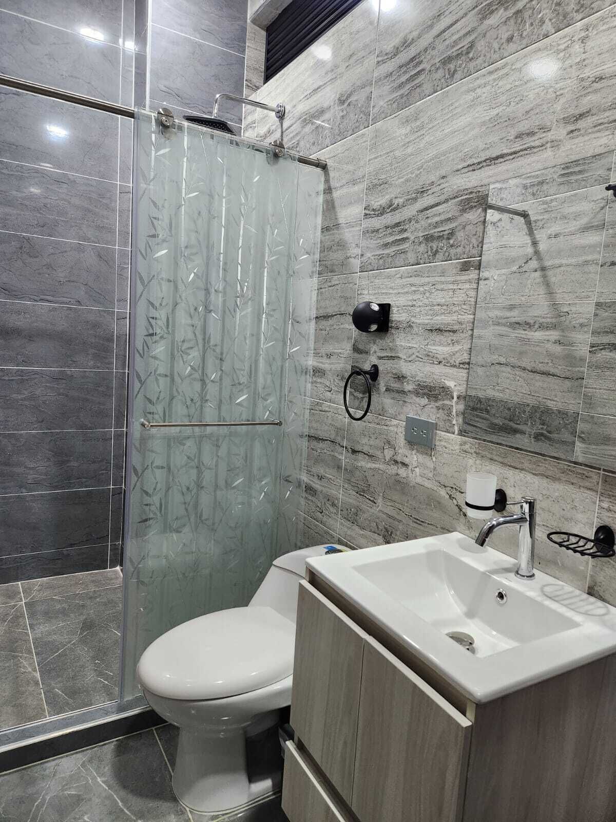 Un baño moderno con cabina de ducha de vidrio, inodoro y lavamanos con mueble de madera.